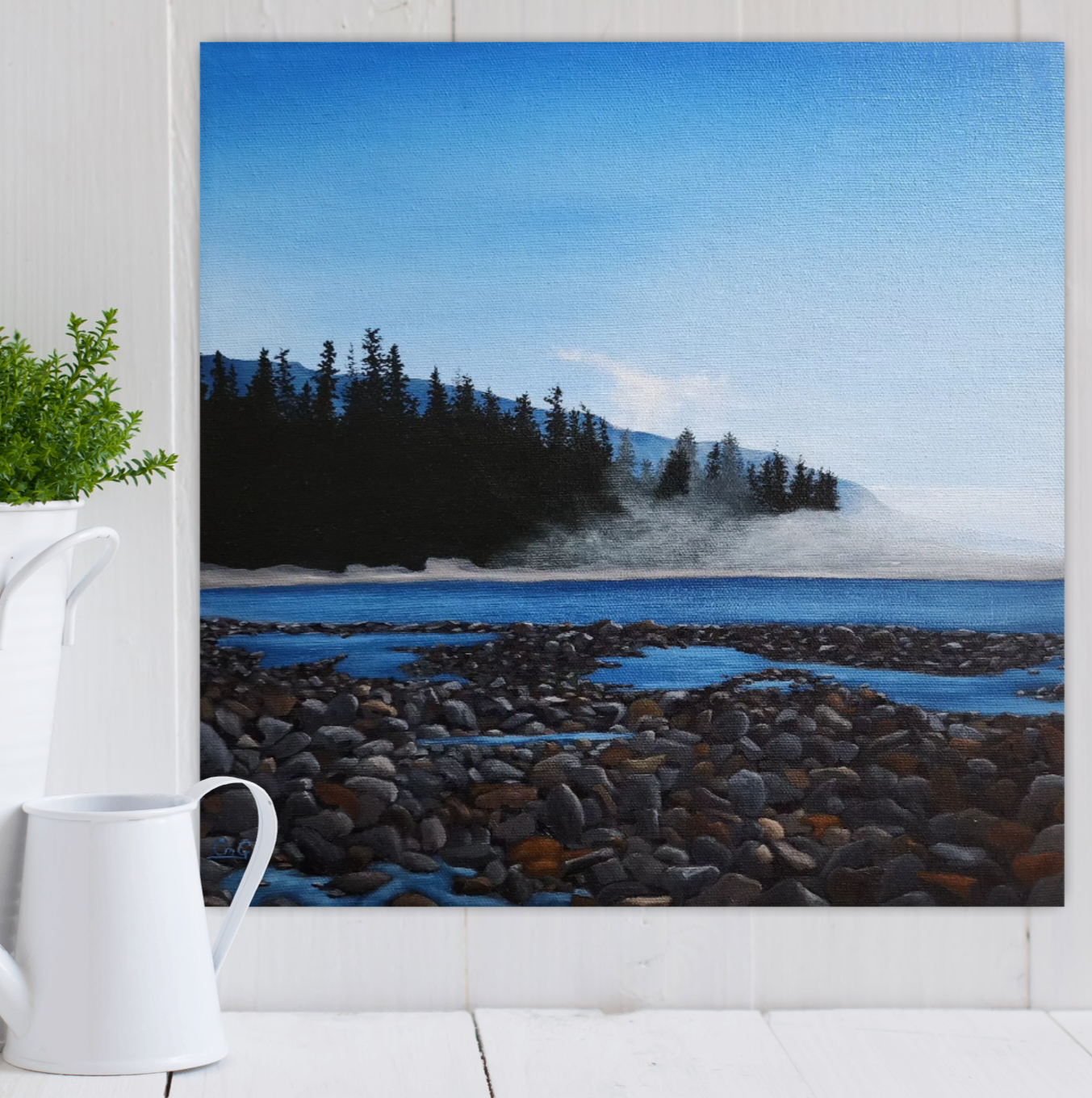 Christina Gouldsborough's Mist's Embrace original landscape painting of Vancouver Island scene hung on a white wall behind a plant and water can on a table