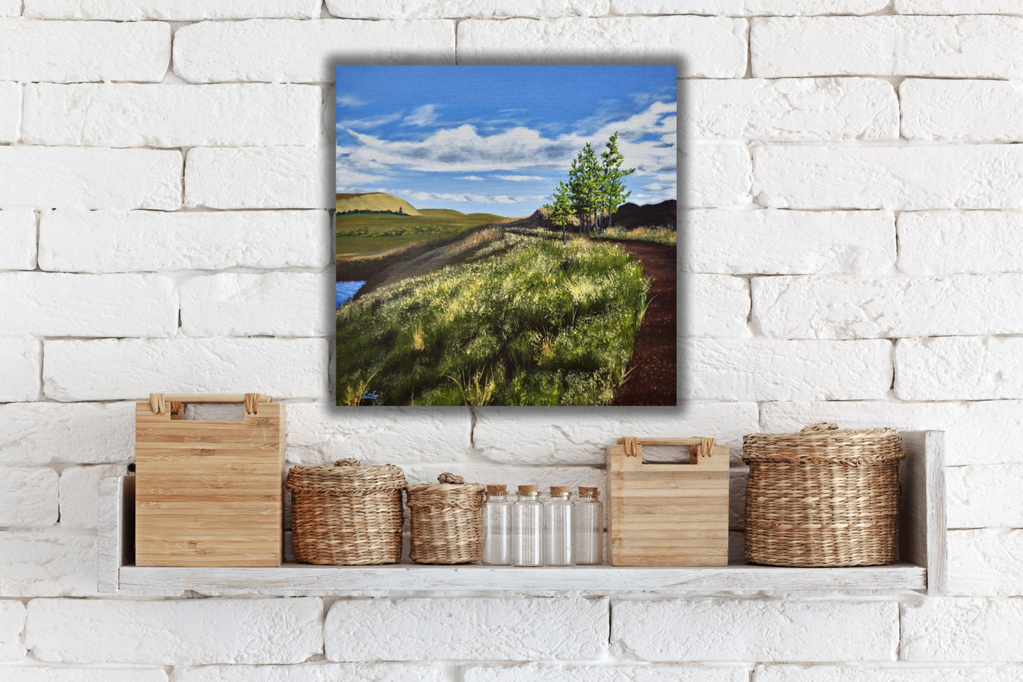 White brick wall with shelf of baskets and containers and a landscape painting hanging behind of a path going through the badlands