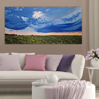 Golden Hour Affirmation is an original oil painting by Christina Gouldsborough of a vibrant stormy sky with a sunset over a canola field on a wall over a white couch and purple and pink cushions