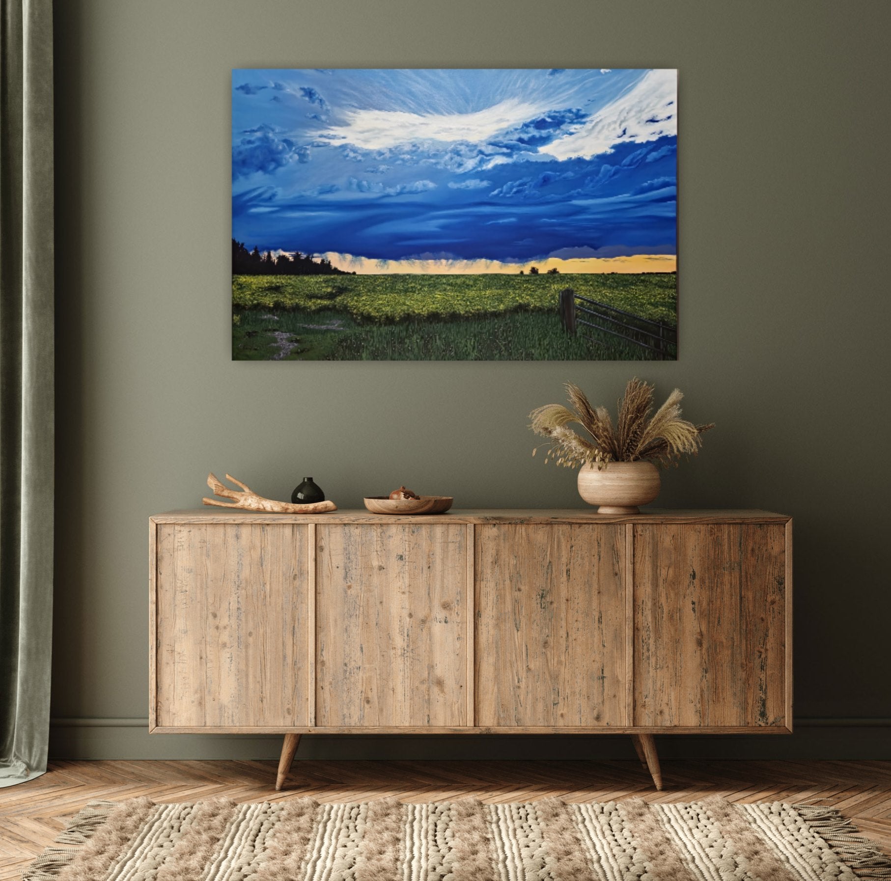 Canola Field At Dusk is an original oil painting of vibrant storm clouds over a beautiful sunset, over the prairie canola fields. Hanging on a green wall behind a console